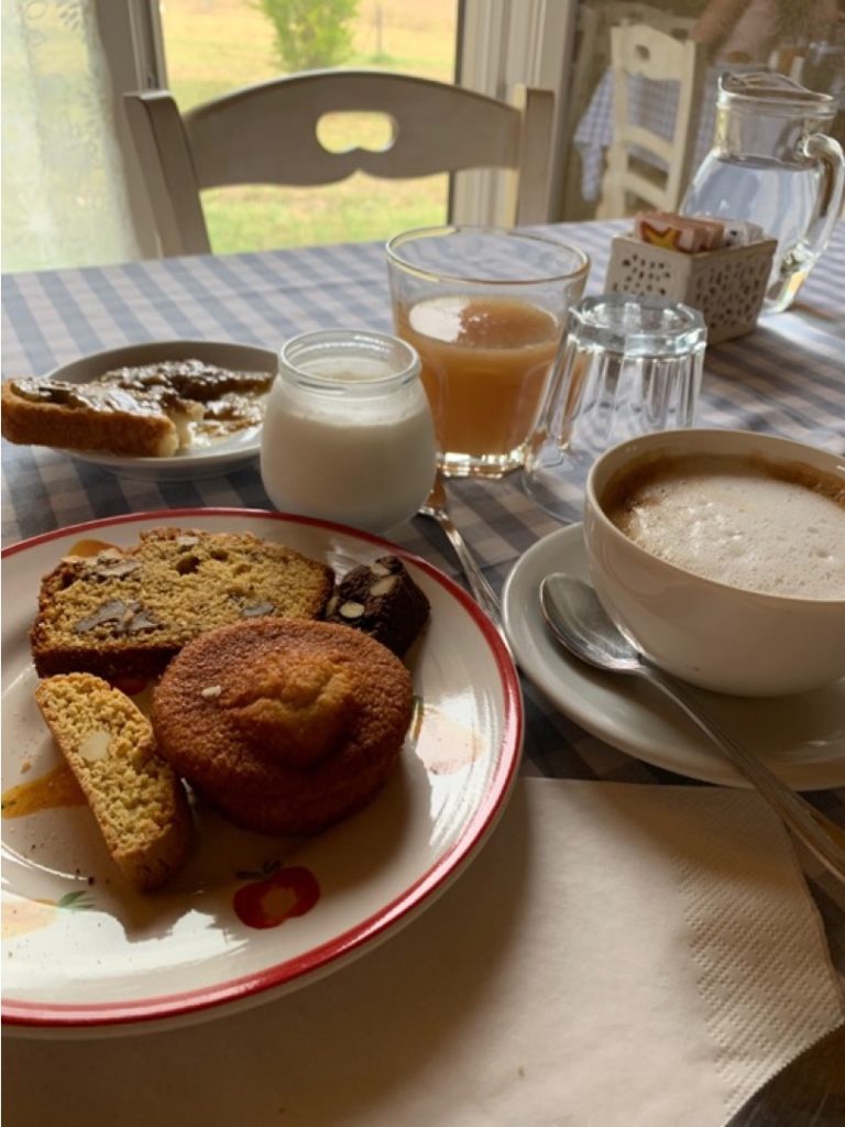 Piatto di dolci per colazione, bicchiere di spremuta e tazza di cappuccino su una tovaglia a quadretti bianchi e azzurri