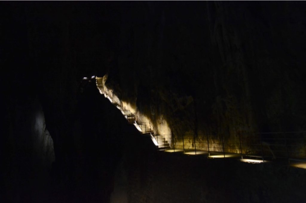 L'interno buio di una grotta, con passerella e scale illuminate