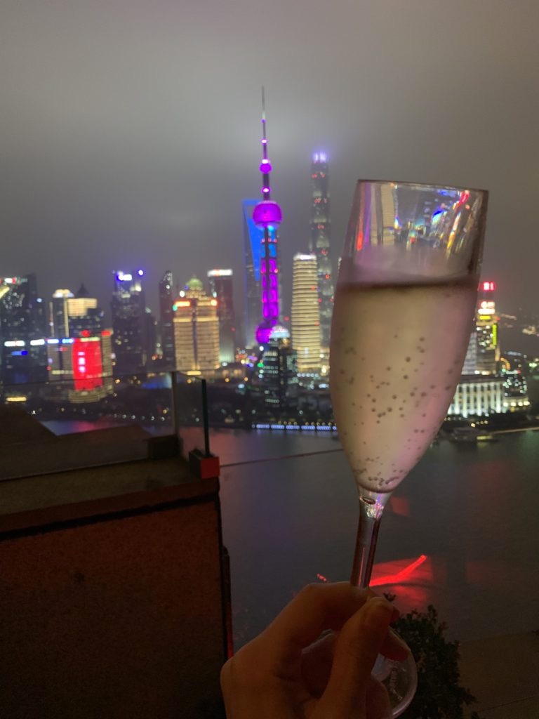 Calice di prosecco in primo piano, sullo sfondo i grattacieli di Shanghai illuminati di notte