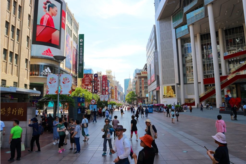 Via affollata di Shanghai di giorno, con negozi e centri commerciali e insegne colorate