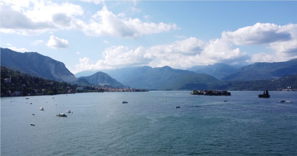 Lago con montagne sullo sfondo, un isolotto al centro e diverse barche