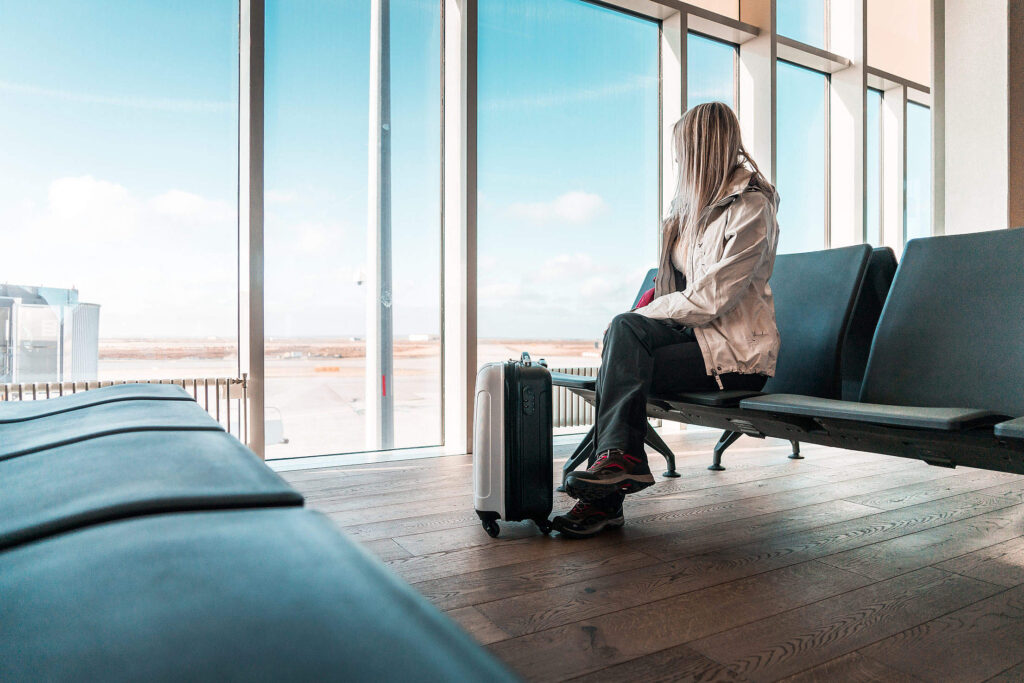 Una ragazza aspetta il suo volo seduta in aeroporto con davanti una piccola valigia