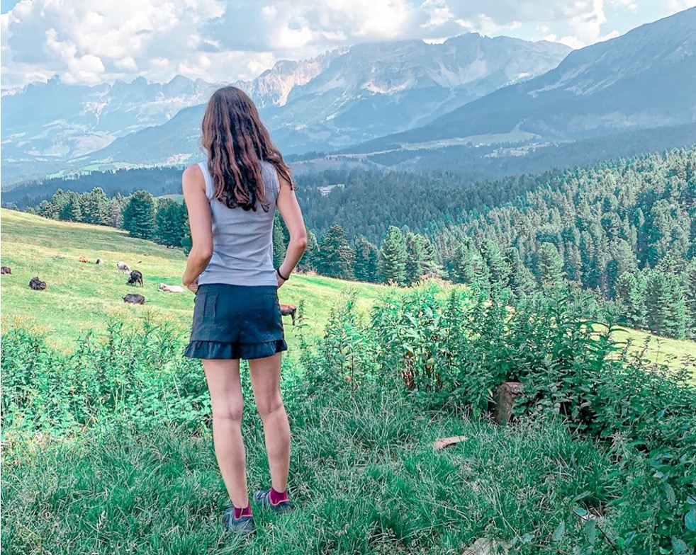 Ragazza di spalle in un prato che guarda le montagne